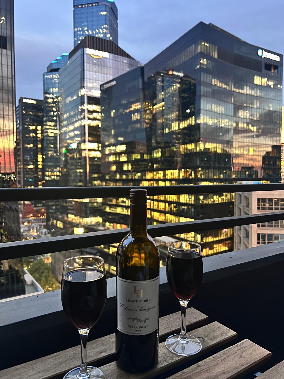Balcony with wine glasses overlooking Melbourne CBD at sunset